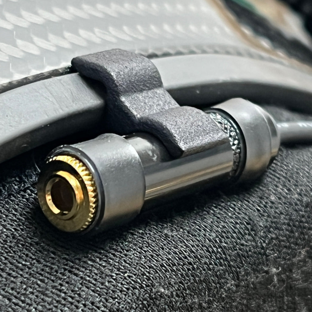Close-up of Trac-Com Ear Bud Clip attached to carbon fiber racing helmet