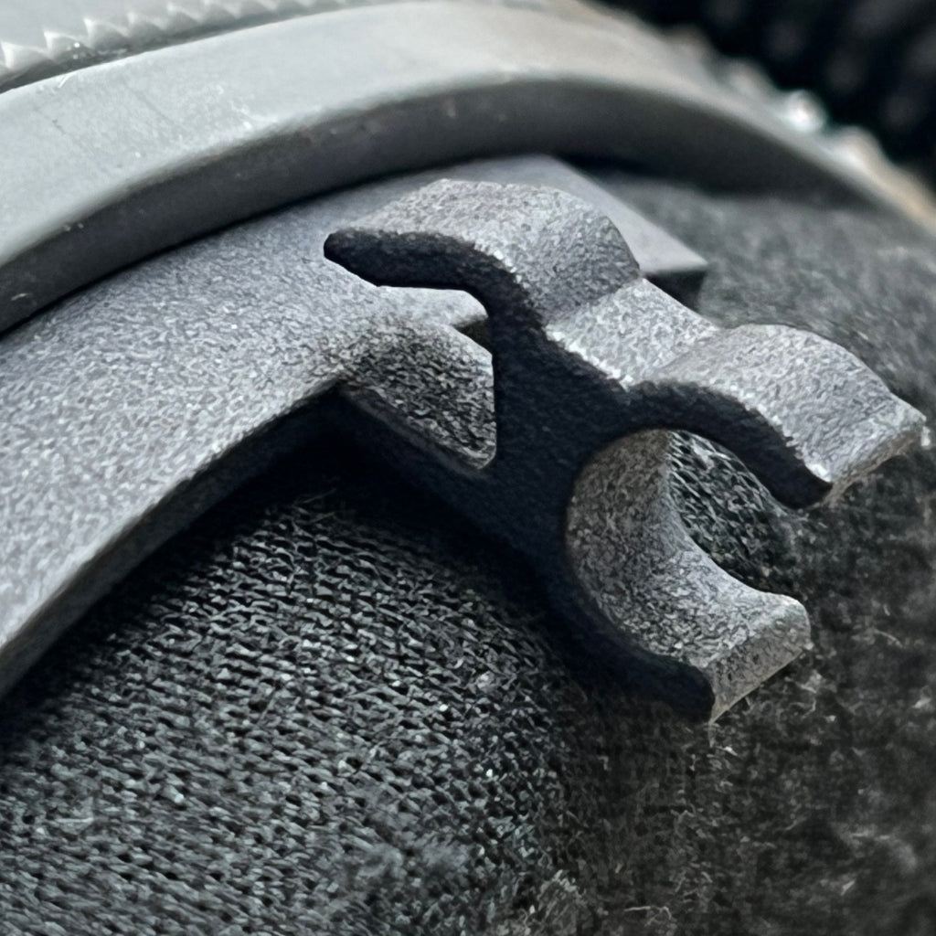 Super close-up of Trac-Com Earbud Connector clip on carbon fiber helmet